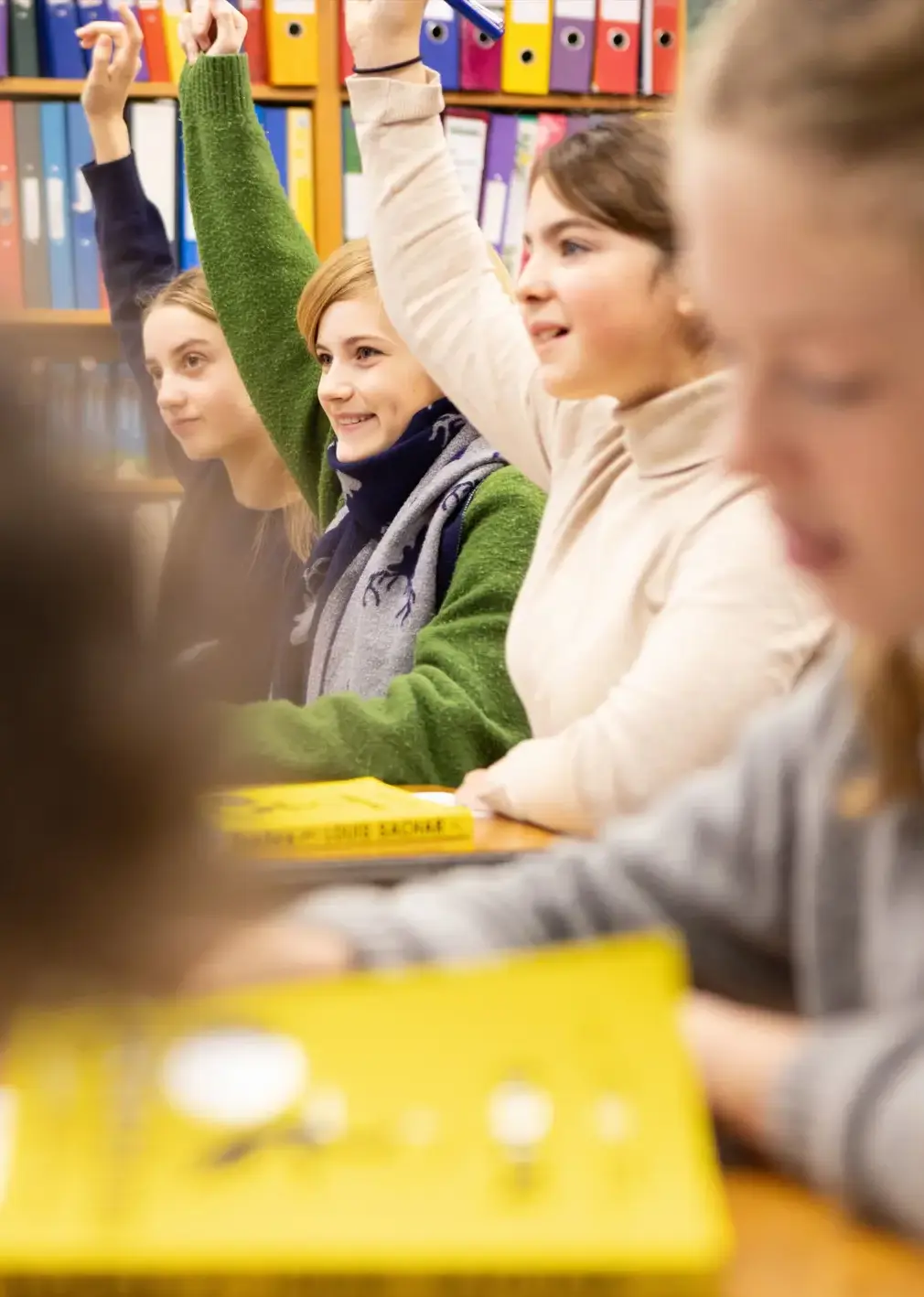 Students Raising Hands in Class With Books on Their Desks
